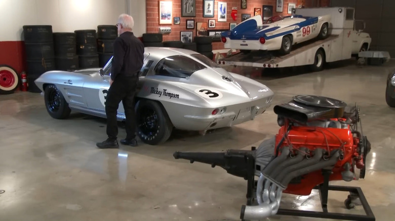 Tom McIntyre stands next to Mickey Thompson's 1963 Chevrolet Corvette Z06 and the 427 Mark-IIS Mystery Motor on a stand in a garage.