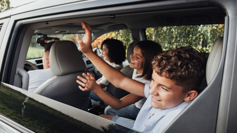 three kids wave out the window of a minivan