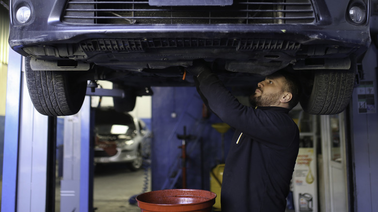 A mechanic drains the oil from a car resting on a lift.