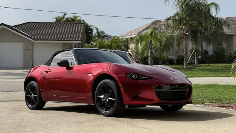 A red Miata parked in a driveway in florida on a clear sunny day.