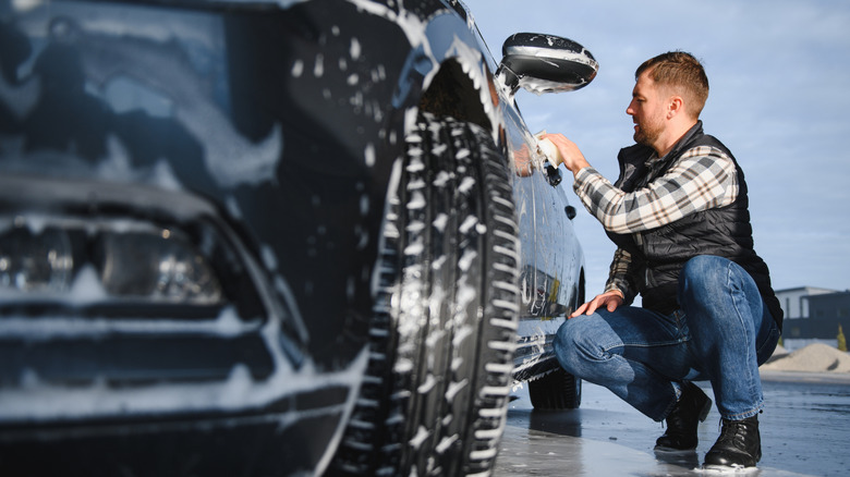A man in a plaid shirt washing a car