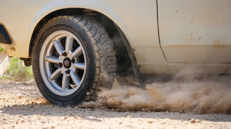 A close up of a tire kicking up dust as the car is pushed hard