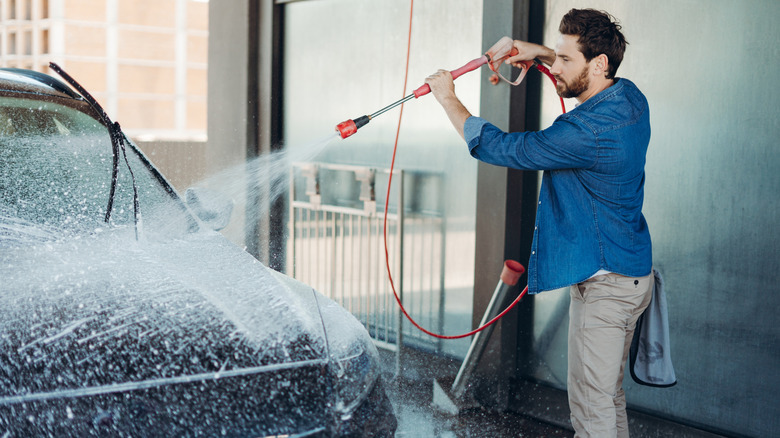 A man in a jean shirt washing his car at a car wash