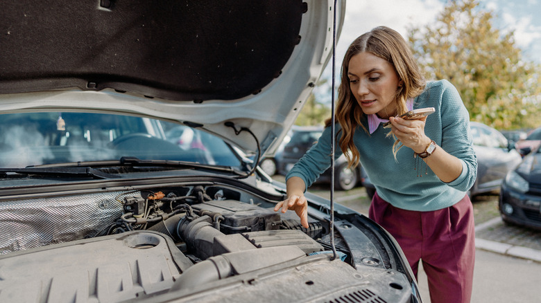 Woman speaking on a cell phone while inspecting her car engine