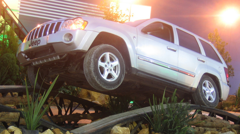 A silver WK Jeep Grand Cherokee drives over an axle articulation demonstration at an auto show