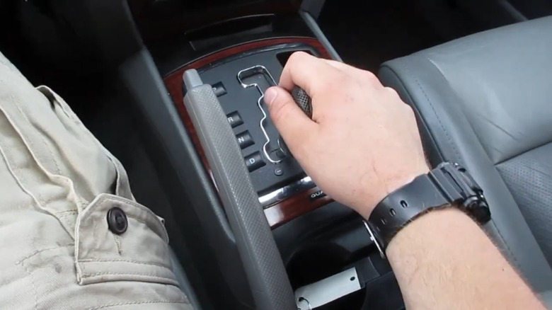 A close-up of a man's hand with a black wristwatch, shifting the AutoStick on a WK 2006 Jeep Grand Cherokee Limited 5.7 Hemi