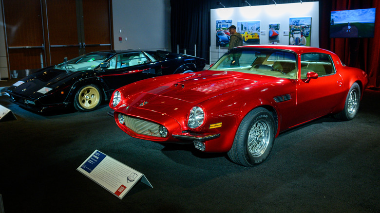 The reddish Pontiac Pegasus parked adjacent to a achromatic Lamborghini Countach successful a museum