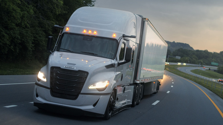 A fifth-gen Freightliner Cascadia driving on a highway at dusk.