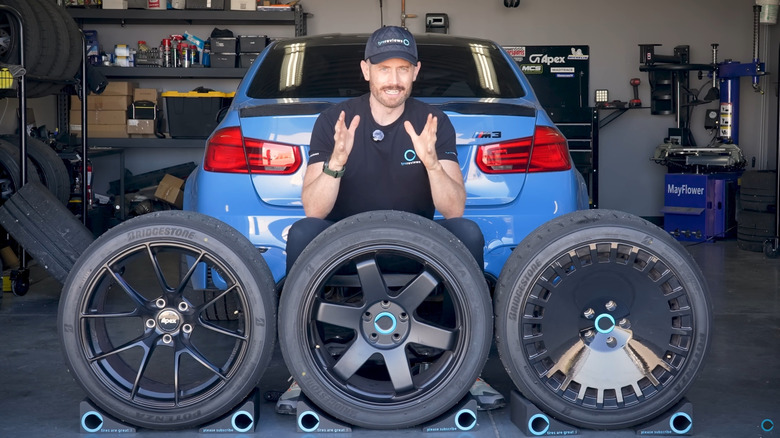 Tyre Reviews' Jonathan Benson with three rims each weighing more than the last, sits in front of his blue F80 BMW M3 in his garage