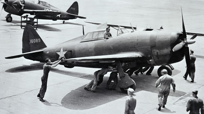 A black-and-white photograph of a P-47 Thunderbolt airplane being pushed connected nan runway by a attraction crew
