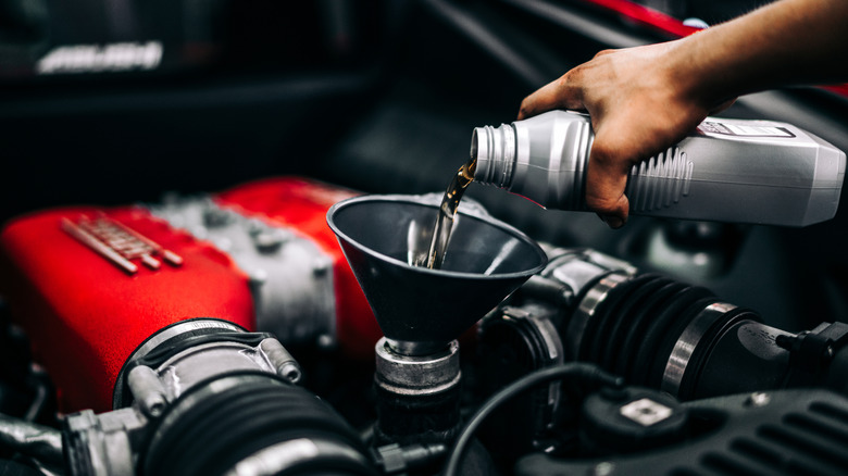A person pouring a fresh oil into an engine