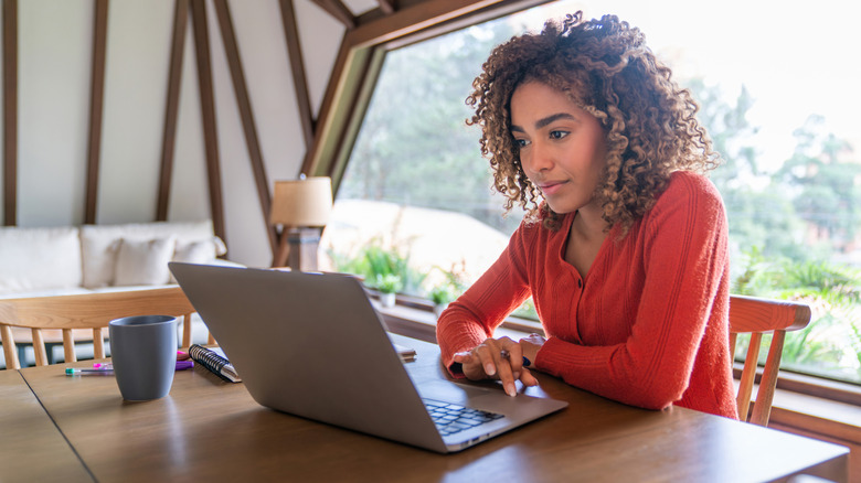 A woman does research on a laptop by a window.