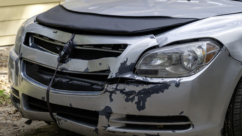 A close-up of a heavily damaged front end of a silver car.