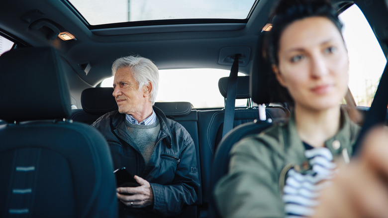 A man rides in the back seat while a woman drives.