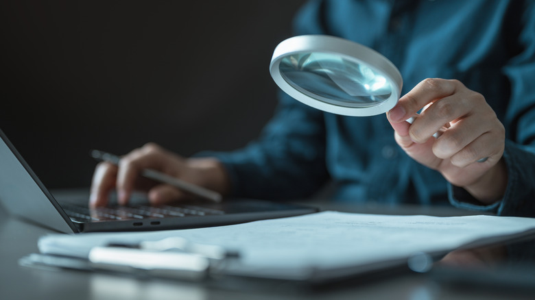 A person uses a magnifying glass to look at paperwork.