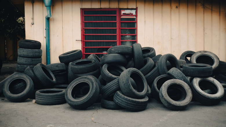 Pile of used tires sitting on the ground by a building