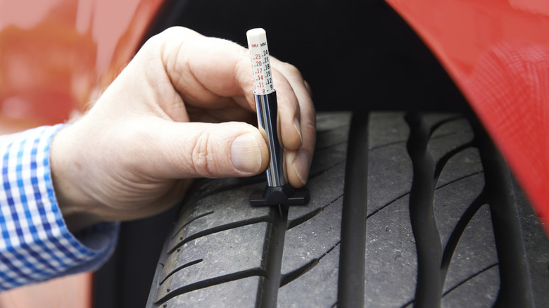 Man checking the tread depth of a car tire using a gauge