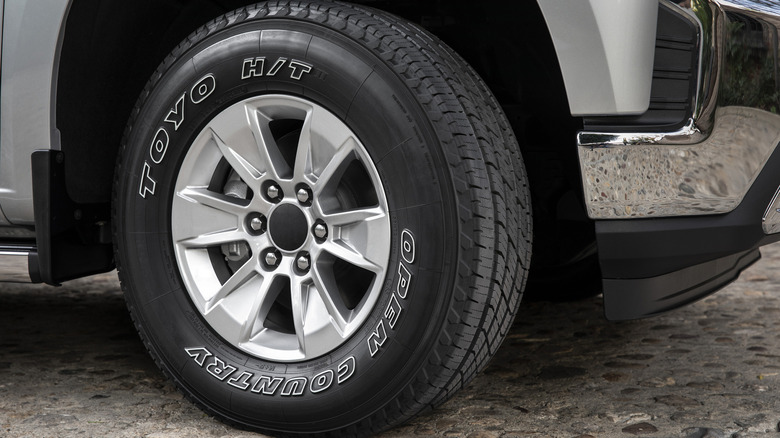 A close-up of a Toyo Open Country H/T tire on a silver truck's front wheel parked on a paved stone surface