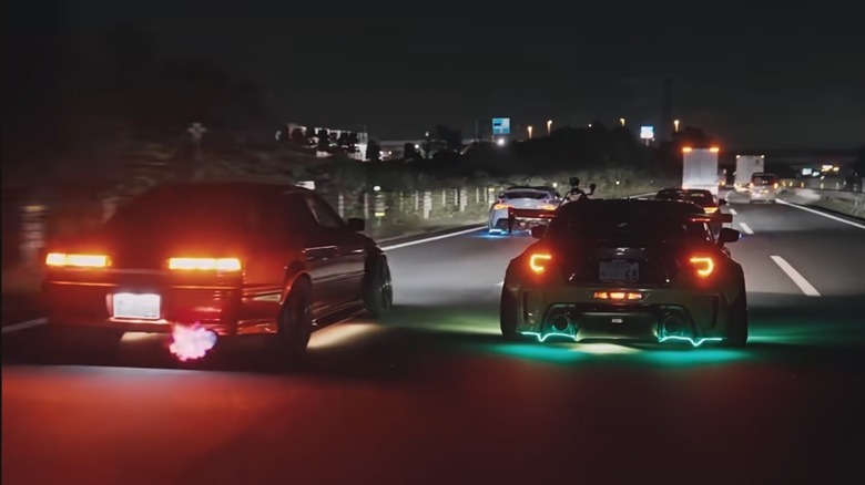 Rear view of four tuner cars with colorful underglow on a highway at night