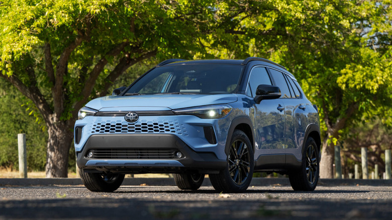 A light blue Toyota Corolla Cross Hybrid XSE crossover with a black roof parked under trees.