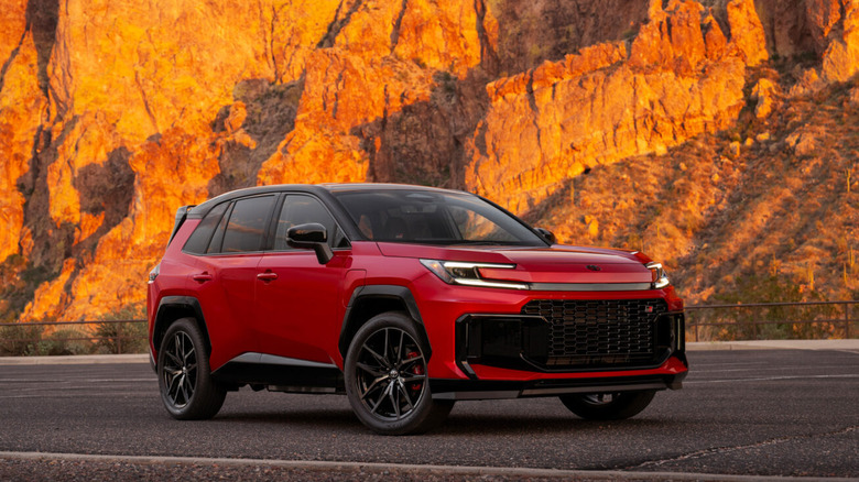 A bright red Toyota RAV4 PHEV GR Sport crossover with black wheels parked in front of desert rock formations.