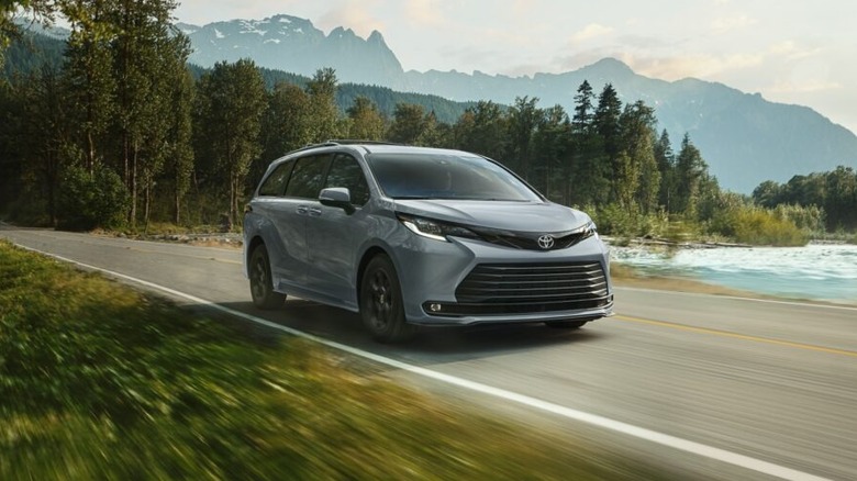 A light grey Toyota Sienna Woodland Edition minivan driving along a scenic mountain road next to a river.