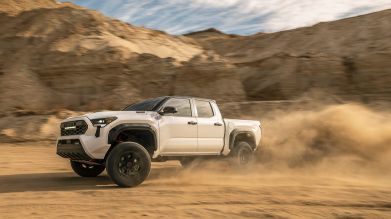 A white Toyota Tacoma TRD Pro pickup truck kicking up a cloud of dust while driving off-road in the desert.