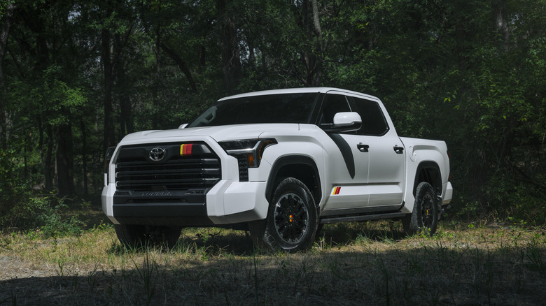 A white Toyota Tundra pickup truck featuring heritage TRD Rally yellow and red stripes parked near a forest.