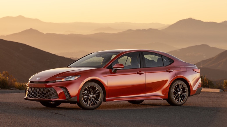A red 2026 Toyota Camry parked on pavement in front of hills.