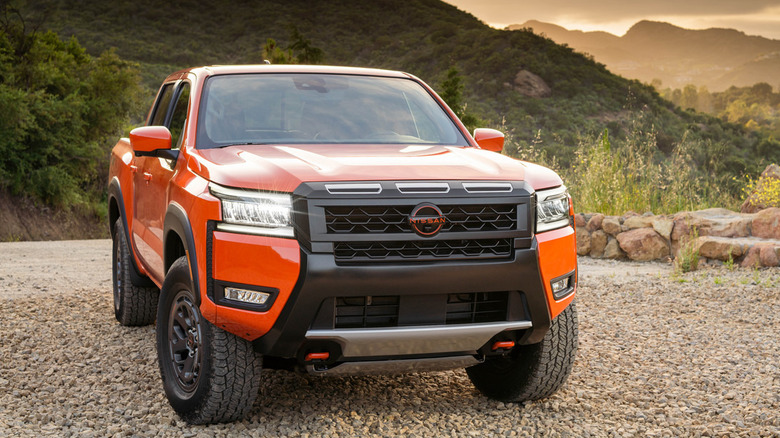 A bright orange Nissan Frontier PRO-4X crew cab pickup truck parked on a gravel path.