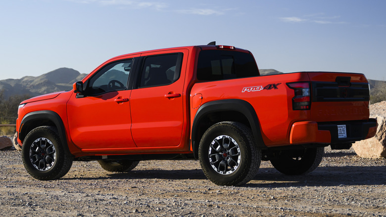 A bright orange Nissan Frontier PRO-4X crew cab pickup truck parked in an open gravel clearing.