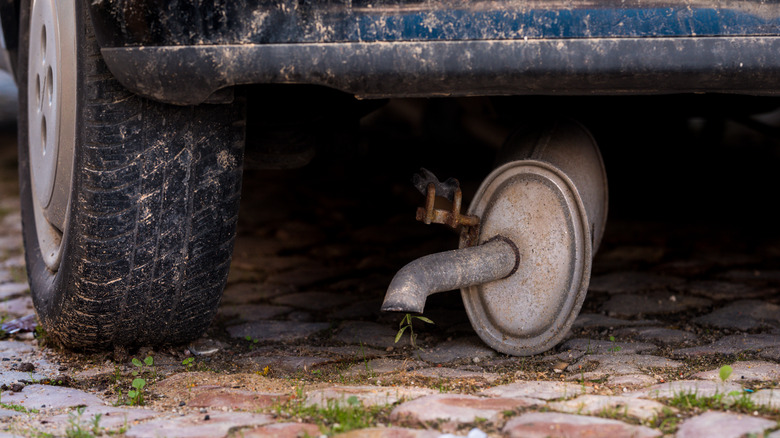 A broken exhaust hanging down on the ground under an old car