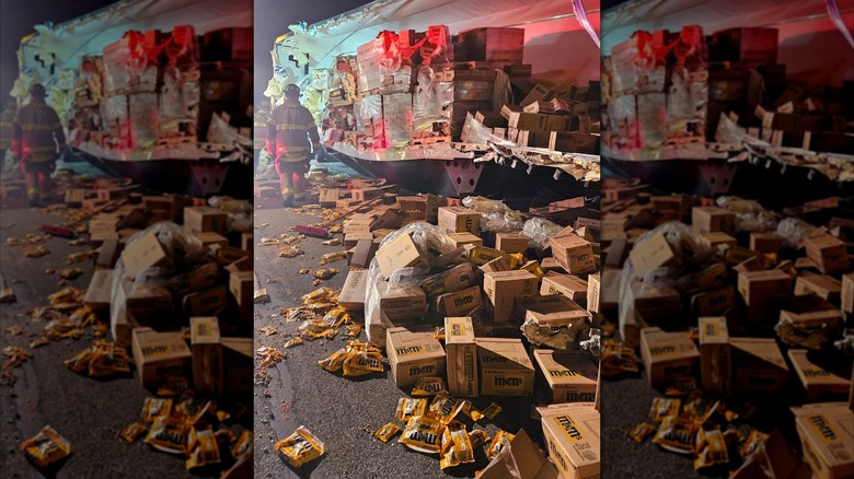A firefighter stands by a trailer with the side ripped off and candy spilled on the highway
