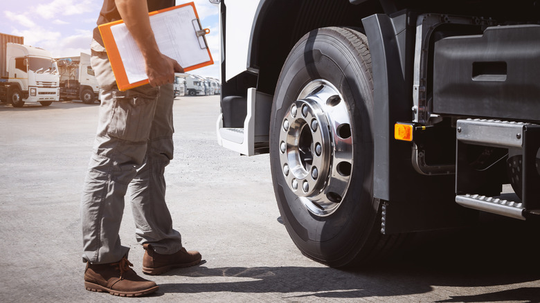 A man with a large clipboard stands next to a semi truck.