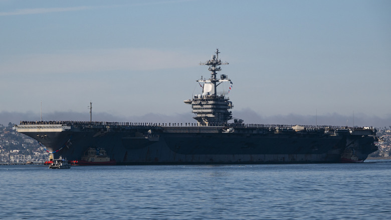 SAN DIEGO, CALIFORNIA - DECEMBER 20: Sailors and marines man the rail as the U.S. Navy Nimitz-class aircraft carrier USS Abraham Lincoln (CVN 72) is guided by tugboats in San Diego Bay as it returns to its homeport of Naval Air Station North Island after a 5-month deployment to the Middle East on December 20, 2024 in San Diego, California. (Photo by Kevin Carter/Getty Images)