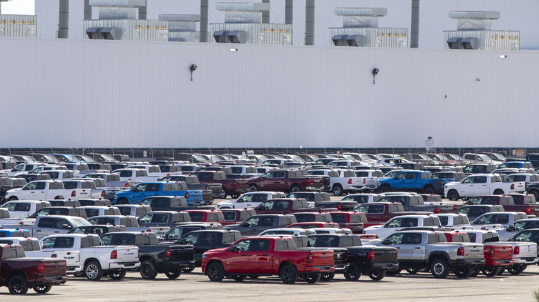 parking lot of a Stellantis plant in Sterling Heights Michigan. A huge lot filled with brand new Ram Trucks of all different colors and trims fills the foreground with the blank gray walls of the factory behind them