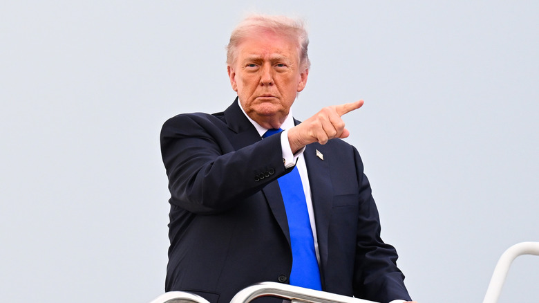 Trump wearing a blue tie pointing to the right, a gray featureless sky in the background