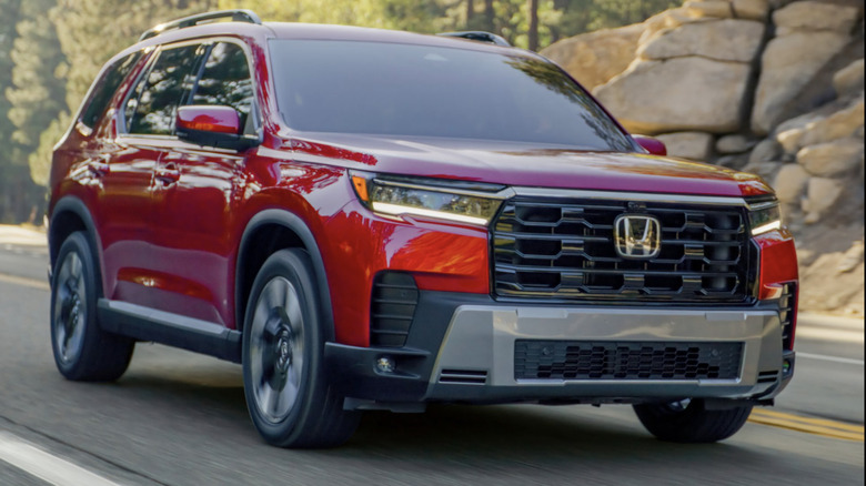 Red Honda Pilot driving down the road with rocks and forrest in the background