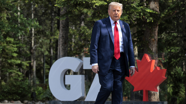 President trump standing in front of a G7 sign with a red maple leaf in the background