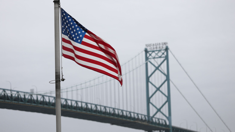 The faded blue Ambassador Bridge sits in the background behind an American flag on a flag pole that is in focus.