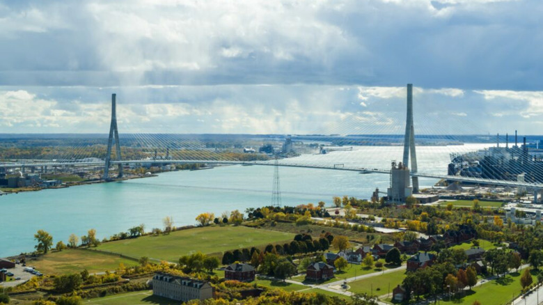 A sunny but cloud-covered day over the Detroit River, revealing sprawling green surrounding the crossing of the Gordie Howe Bridge between Detroit, Michigan and Windsor, Canada.