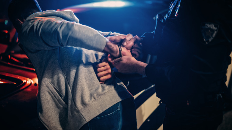 Police pushing a handcuffed man over the hood of a police car