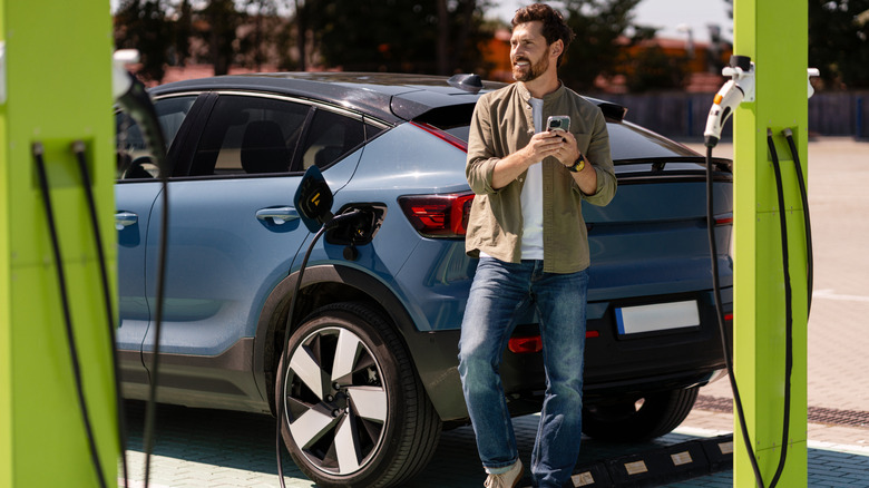 Driver using a smartphone while waiting for an electric vehicle to charge at a modern EV charging station, embracing sustainable transportation