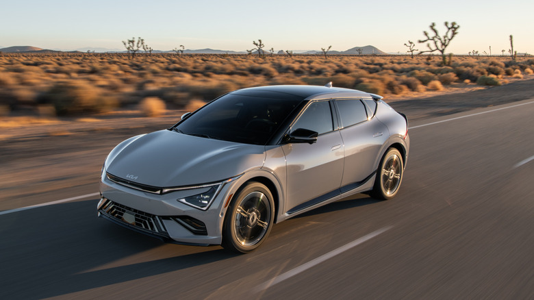 A gray Kia EV6 driving on a desolate desert road in front of shrubs and joshua trees