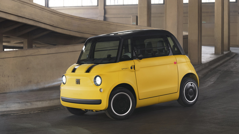 A yellow Topolino Sport driving around a corner in a parking structure with its headlights on