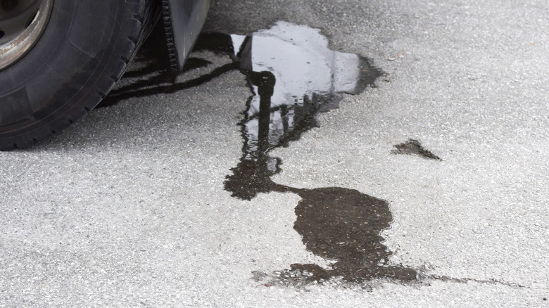 A vehicle tire and mudflap, as well as a fresh oil stain on a concrete driveway