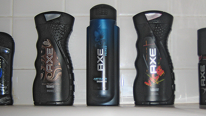 A lineup of Axe body wash, shampoo, shower gel, and deodorant in front of white bathroom tile