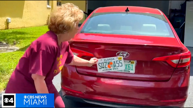 A screenshot showing Nancy holding up the new SQZ A55 plate to the rear of her red Hyundai Sonata parked in her driveway