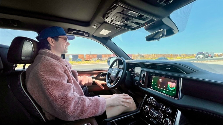 A photo of me wearing a pink fluffy coat behind the wheel of a GMC Yukon with Super Cruise active on the freeway and my hands are on my lap