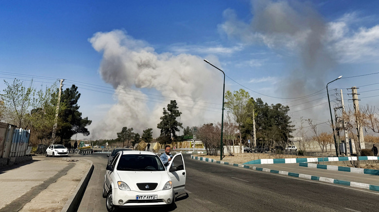 A driver stops as a smoke plume rises after an airstrike on March 5, 2026 in the Boroujerdi Town neighborhood in southern Tehran, Iran.